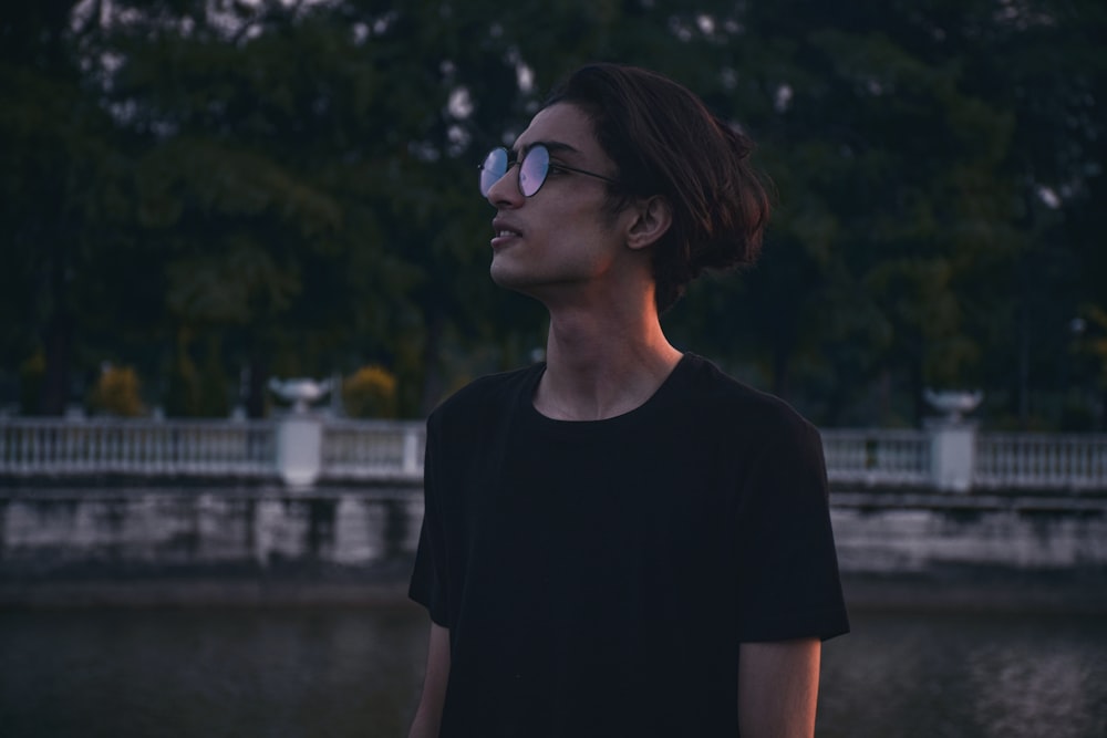 a man wearing sunglasses standing in front of a body of water