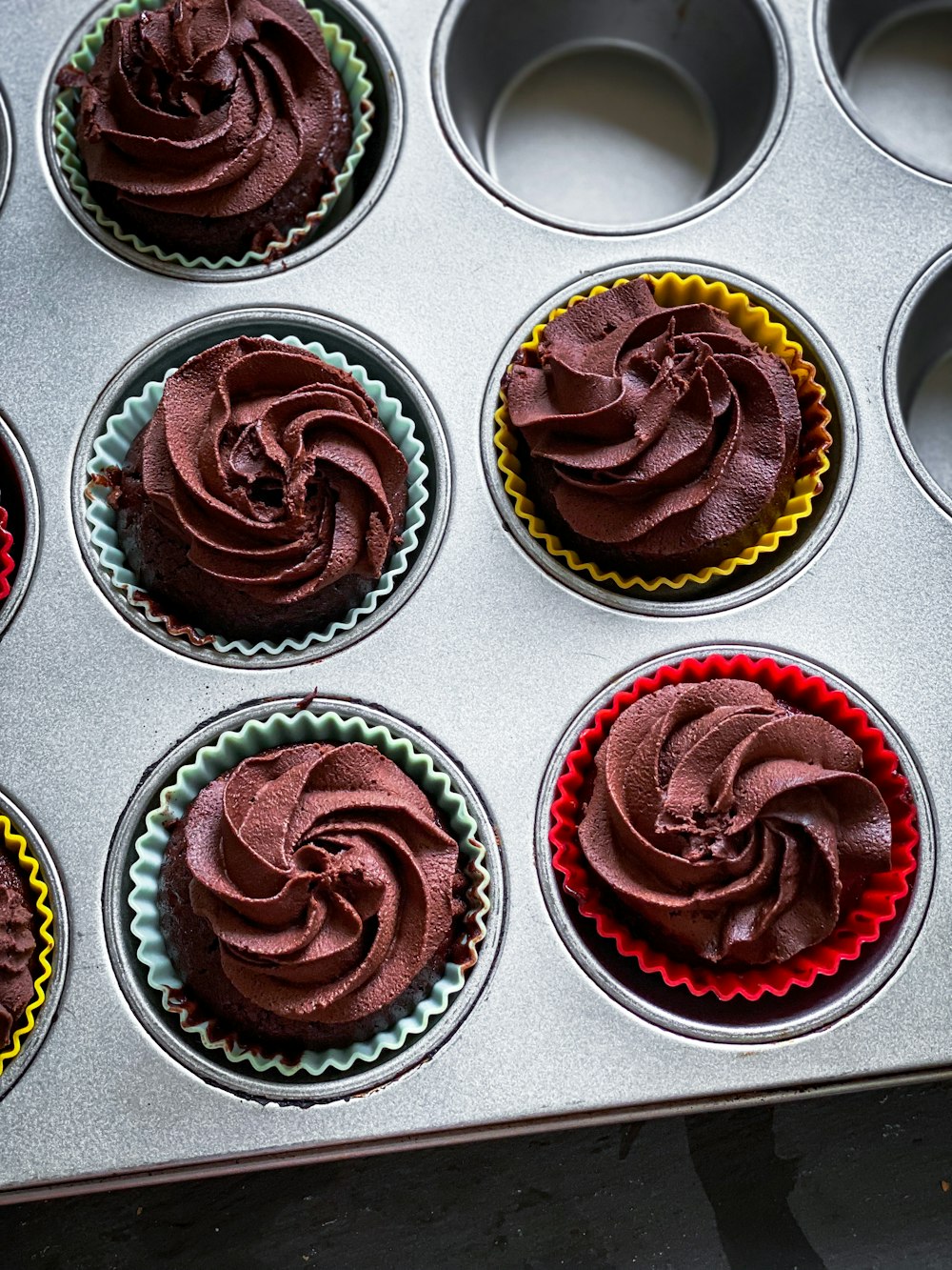 a muffin tin filled with cupcakes covered in chocolate frosting