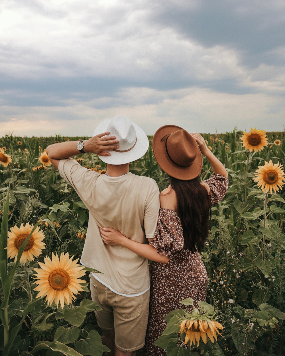 a man and a woman standing in a field of sunflowers