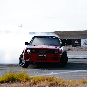 A dynamic shot of a modified JDM car drifting on a racetrack with tire smoke.
