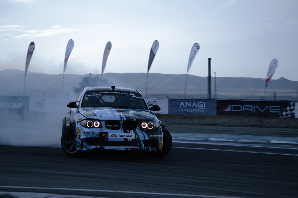 a white car driving down a race track with smoke coming out of it