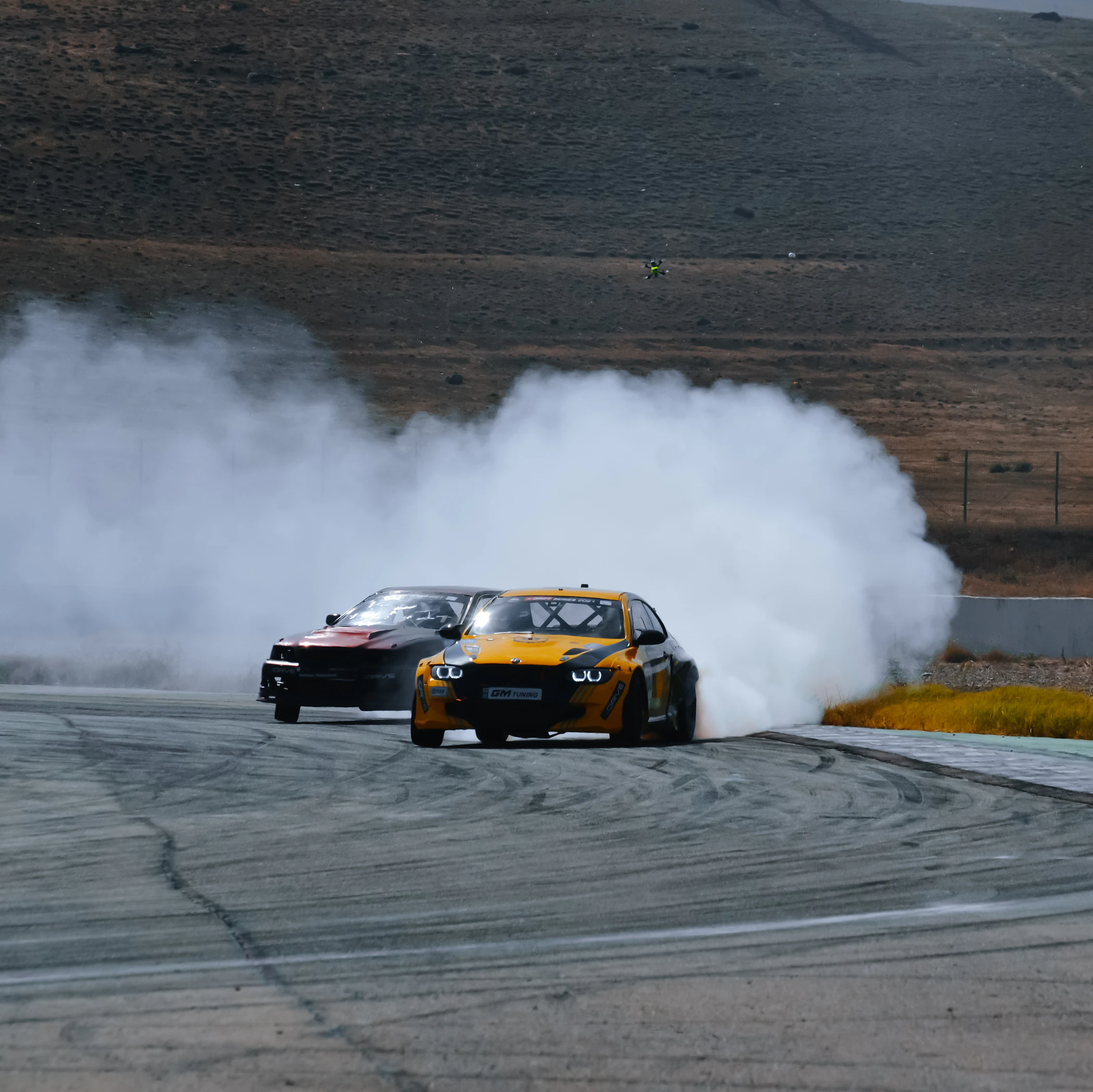 Two drift cars sliding in tandem through tire smoke on a race track