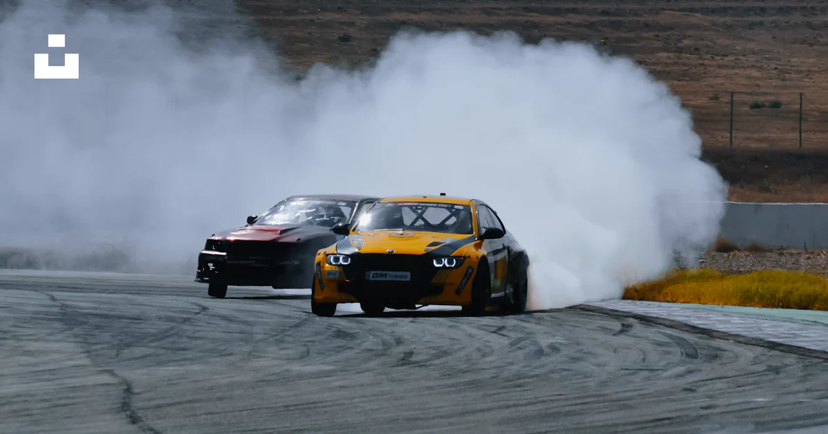 Two cars driving on a race track with smoke coming out of them photo ...