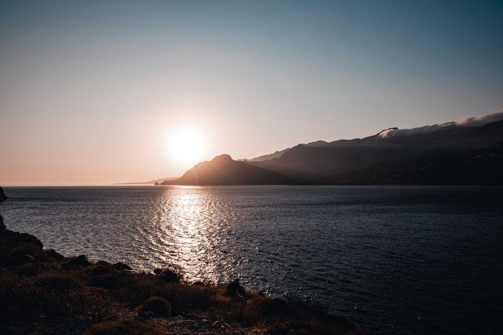 the sun is setting over the ocean with mountains in the background