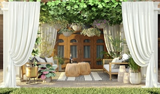 An outdoor seating area features elegant white curtains framing the space. The area is furnished with two wicker chairs and a table, surrounded by vibrant green plants and hanging floral baskets. The wooden doors in the background add a warm touch, while a striped rug adds texture to the floor.