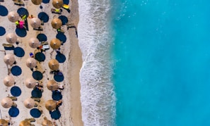 Aerial view of Miami Beach’s white sandy shore and turquoise waters, dotted with colorful umbrellas and sunbathers