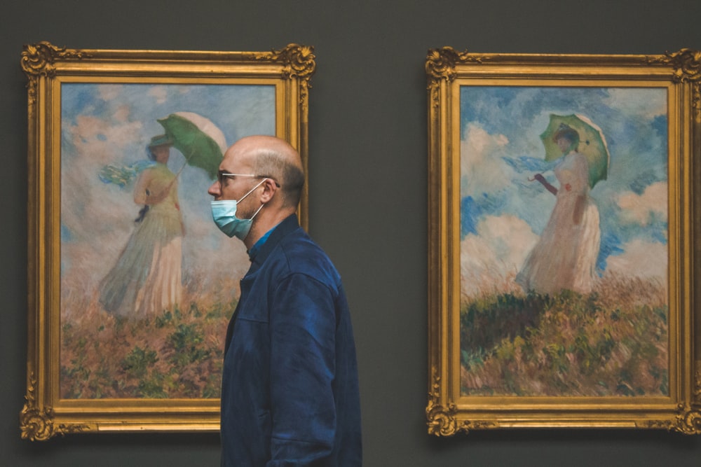 a man wearing a face mask standing in front of two paintings