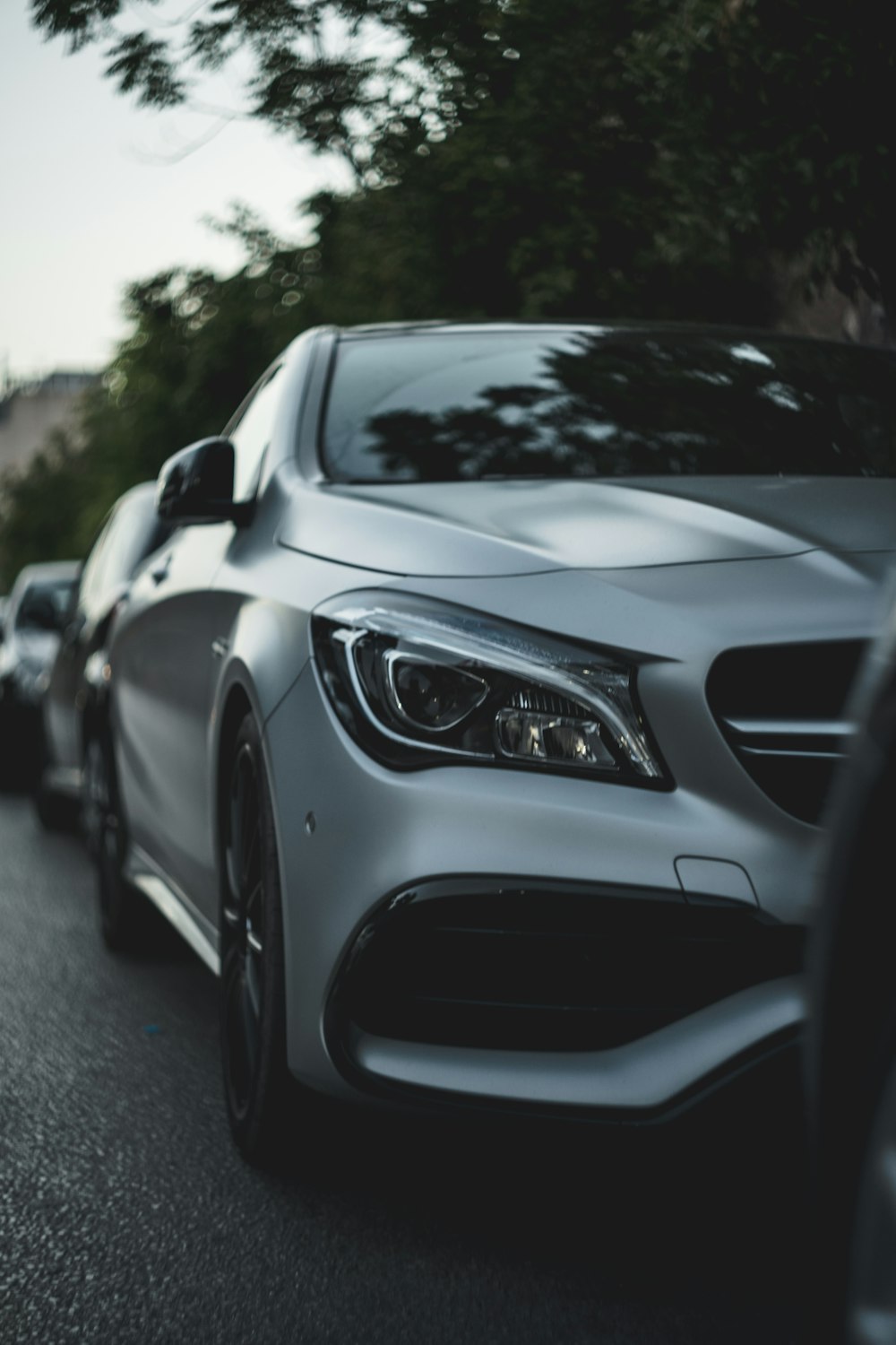 a silver car driving down a street next to a forest