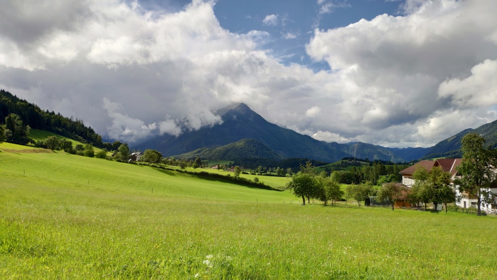 a lush green field surrounded by mountains under a cloudy sky