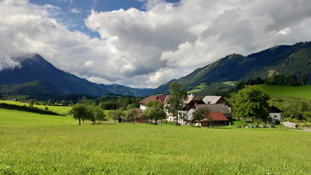 a green field with a house and mountains in the background