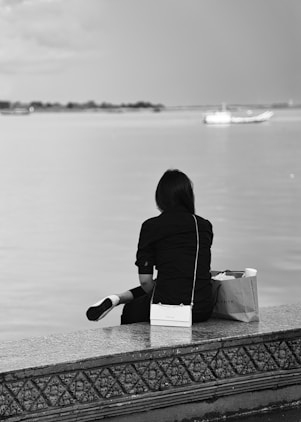 a woman sitting on a ledge looking out at the water