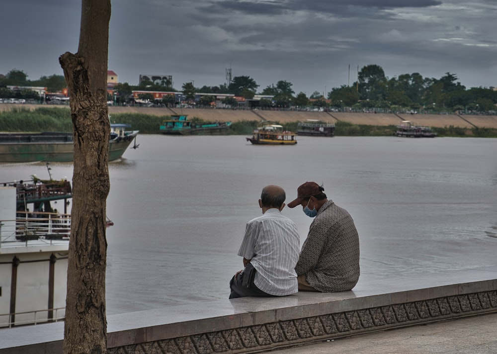 two men sitting on a ledge looking out over a body of water