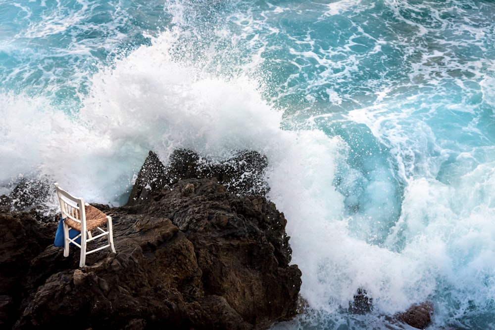 a chair sitting on top of a rock next to the ocean