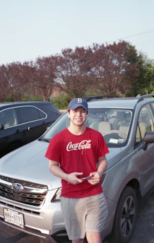 A smiling young adult receiving a quick insurance quote on a smartphone beside a sleek car.