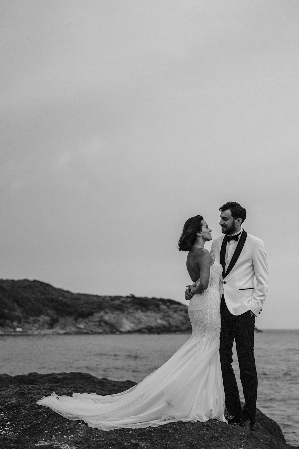 a bride and groom standing on a rock by the ocean