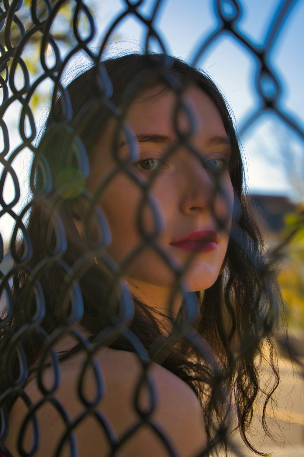a woman looking through a chain link fence