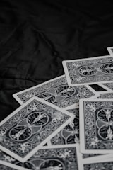 A pile of playing cards featuring intricate, symmetrical patterns on their backs, placed on a dark surface.