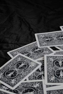 A pile of playing cards featuring intricate, symmetrical patterns on their backs, placed on a dark surface.