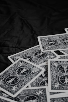 A pile of playing cards featuring intricate, symmetrical patterns on their backs, placed on a dark surface.
