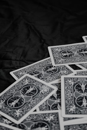 A pile of playing cards featuring intricate, symmetrical patterns on their backs, placed on a dark surface.