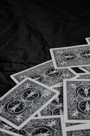 A pile of playing cards featuring intricate, symmetrical patterns on their backs, placed on a dark surface.