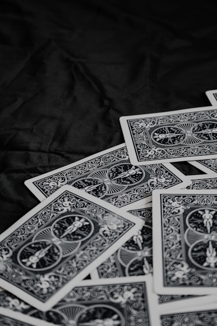 A pile of playing cards featuring intricate, symmetrical patterns on their backs, placed on a dark surface.