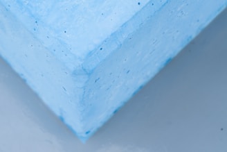 Close-up view of a corner of a textured, light blue foam block appearing to slightly hover over a neutral gray surface.