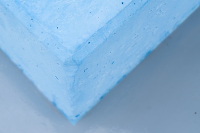 Close-up view of a corner of a textured, light blue foam block appearing to slightly hover over a neutral gray surface.