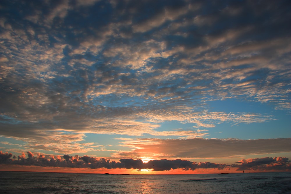 the sun is setting over the ocean on a cloudy day