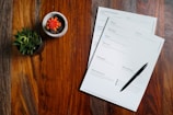 a wooden table topped with papers and a pen