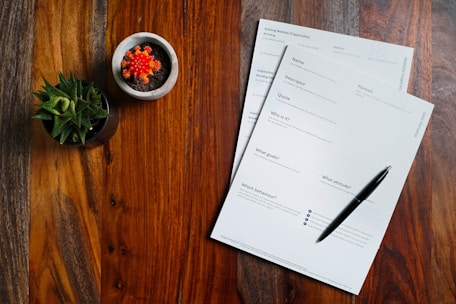 a wooden table topped with papers and a pen