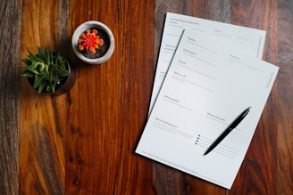 a wooden table topped with papers and a pen