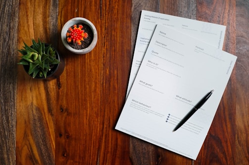 a wooden table topped with papers and a pen
