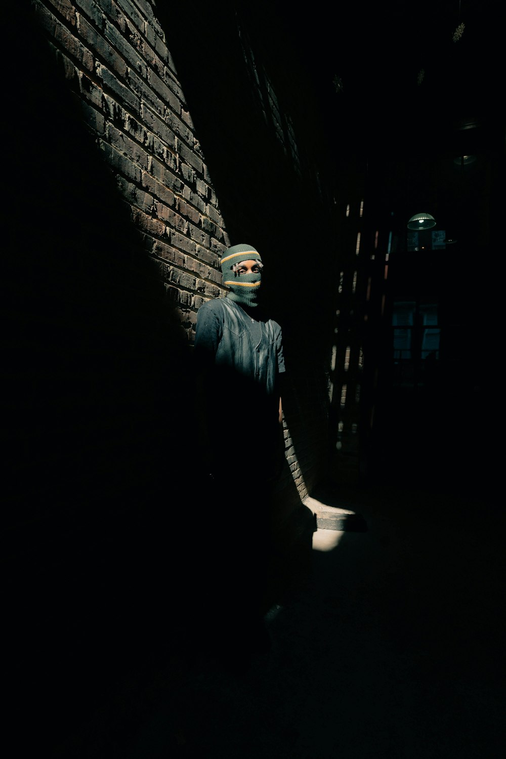 a person with a mask on standing next to a brick wall