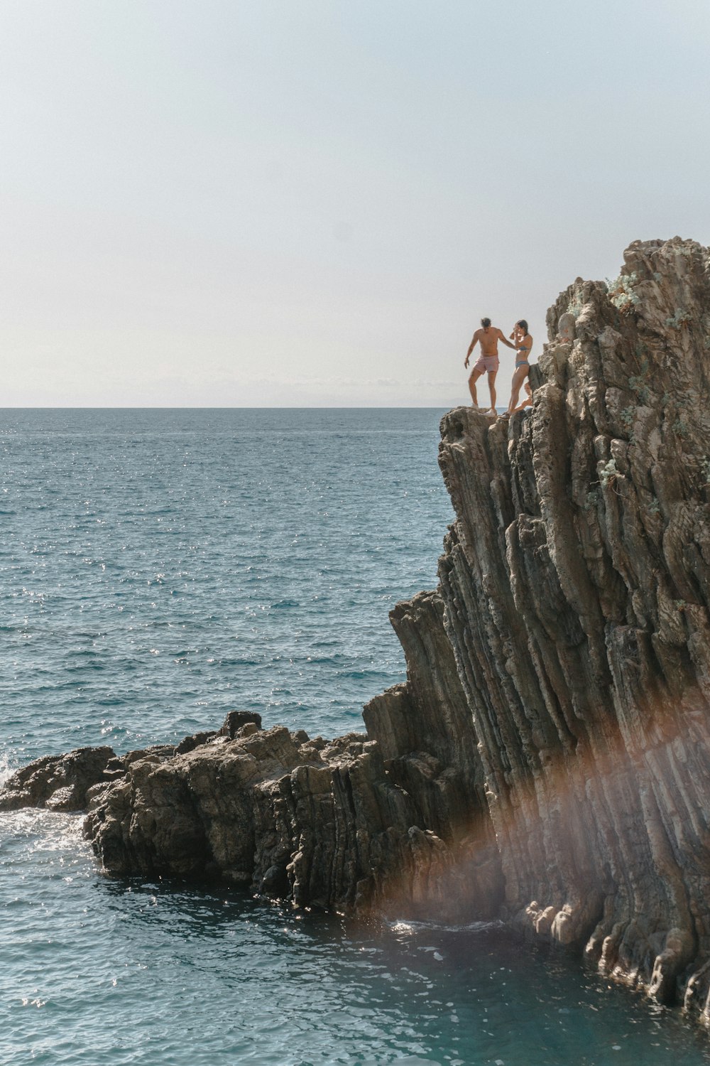 a couple of people standing on top of a cliff next to the ocean