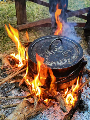 Close-up of sizzling campfire stew bubbling in a rustic cast iron pot over glowing embers.
