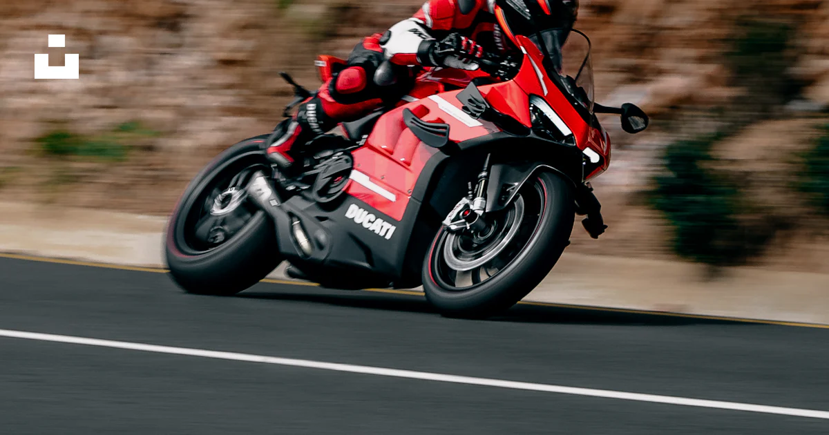 A man riding a red motorcycle down a curvy road photo – Free Ducati ...
