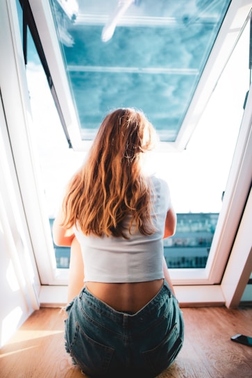 a woman sitting on the floor looking out a window