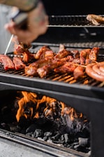 a person grilling hot dogs and sausages on a grill