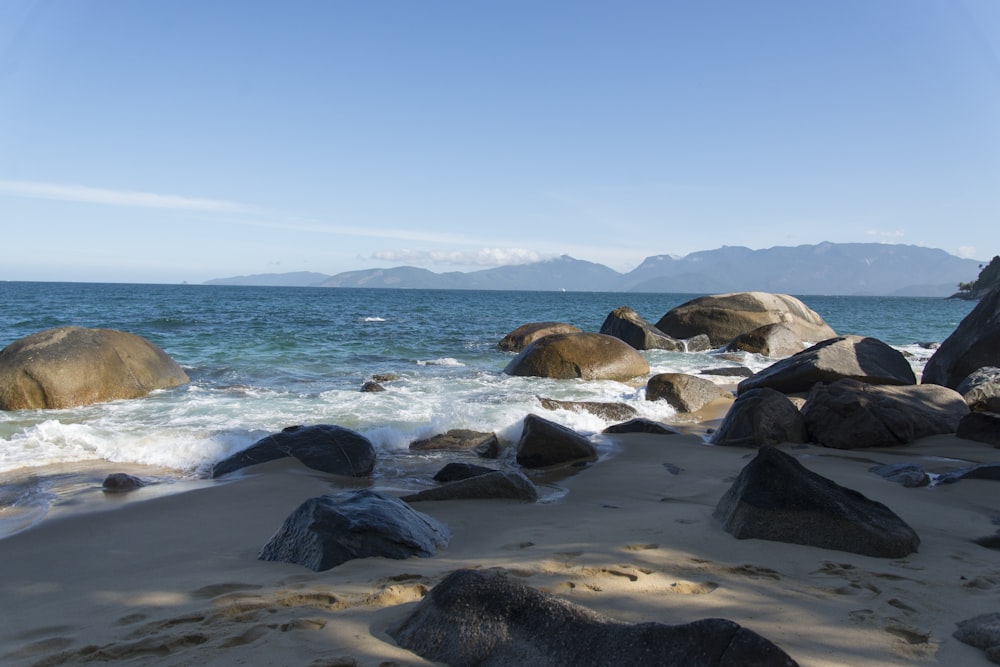 a sandy beach with large rocks in the water