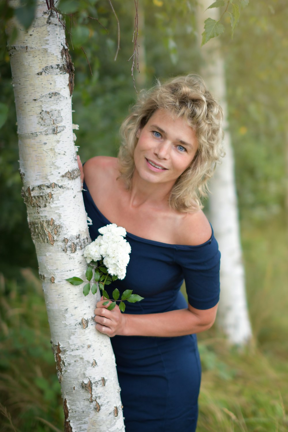 a woman standing next to a tree holding a bouquet of flowers