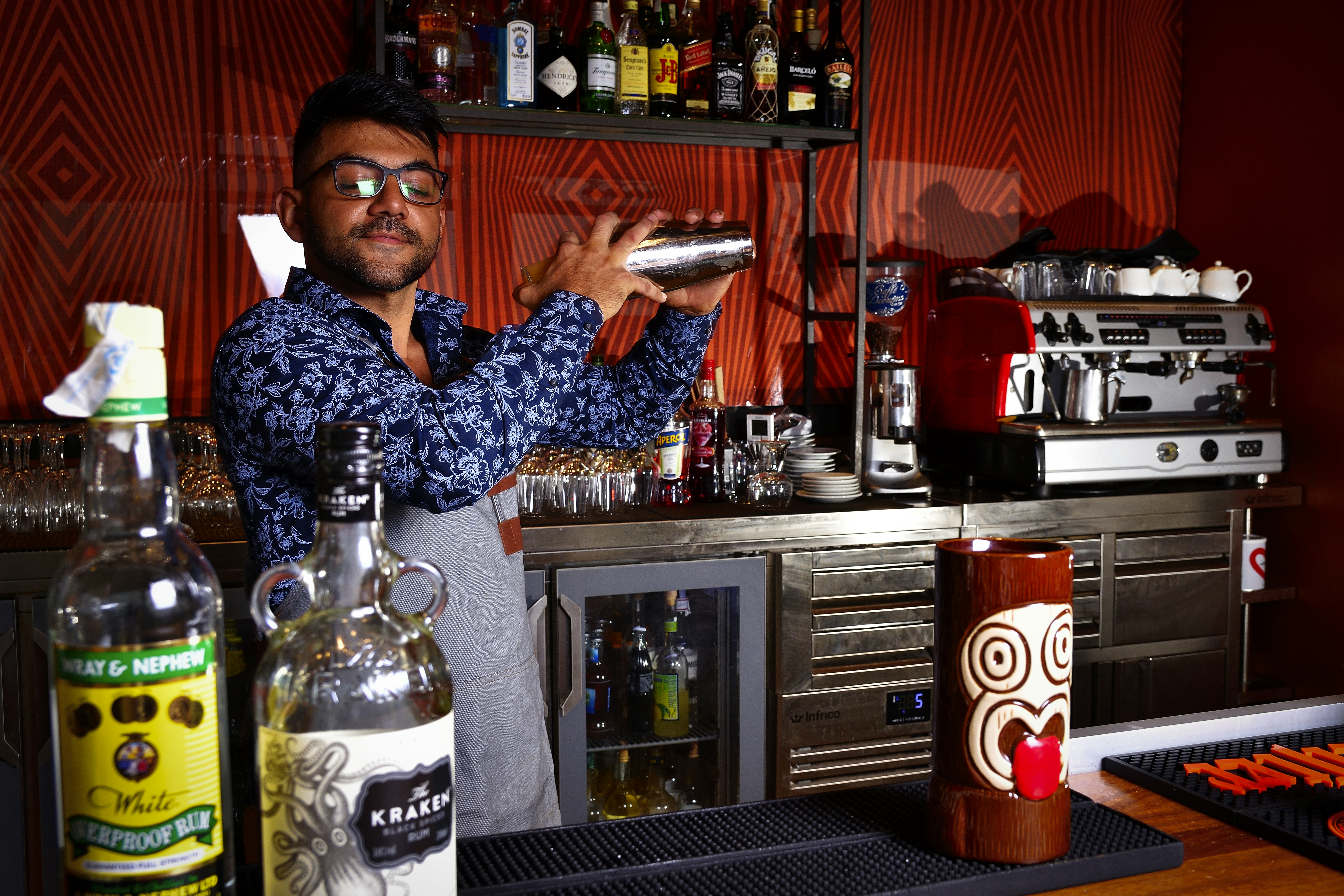 a man standing in front of a bar making a drink