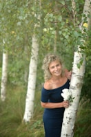 a woman standing next to a tree holding a bouquet of flowers