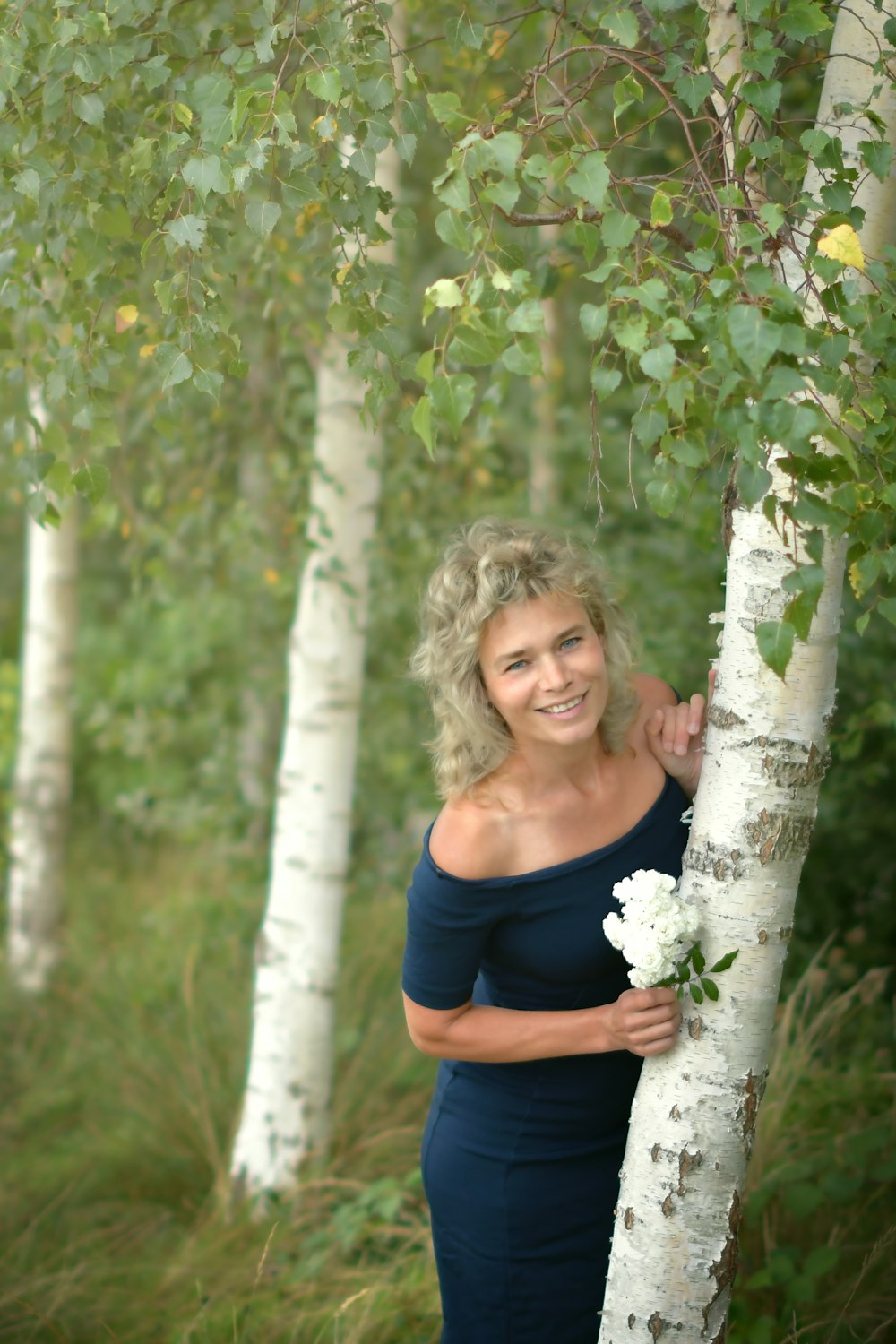 a woman standing next to a tree holding a bouquet of flowers