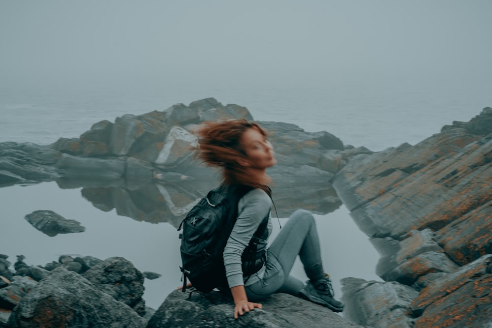 a woman with red hair sitting on a rock by the ocean