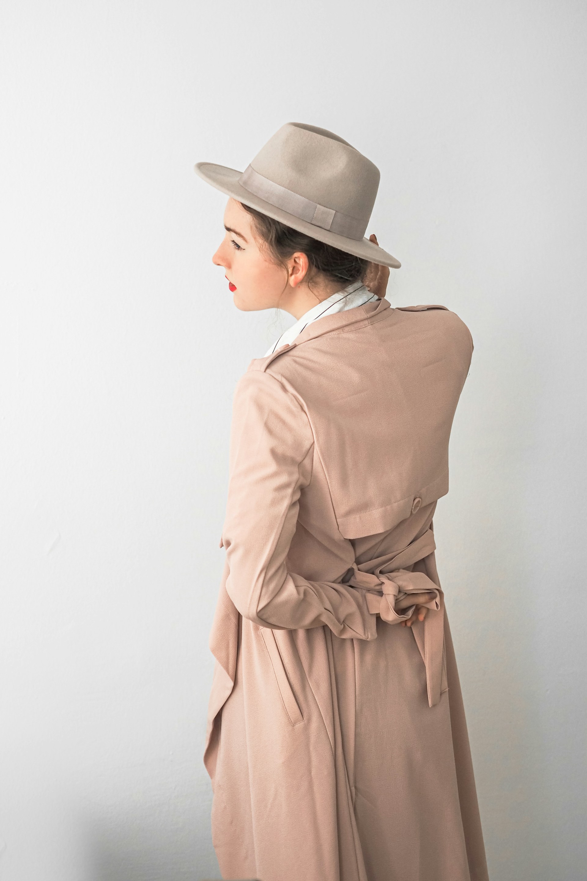 A sleek model wearing a flowing beige trench coat paired with crisp white trousers, standing against a minimalist urban backdrop.