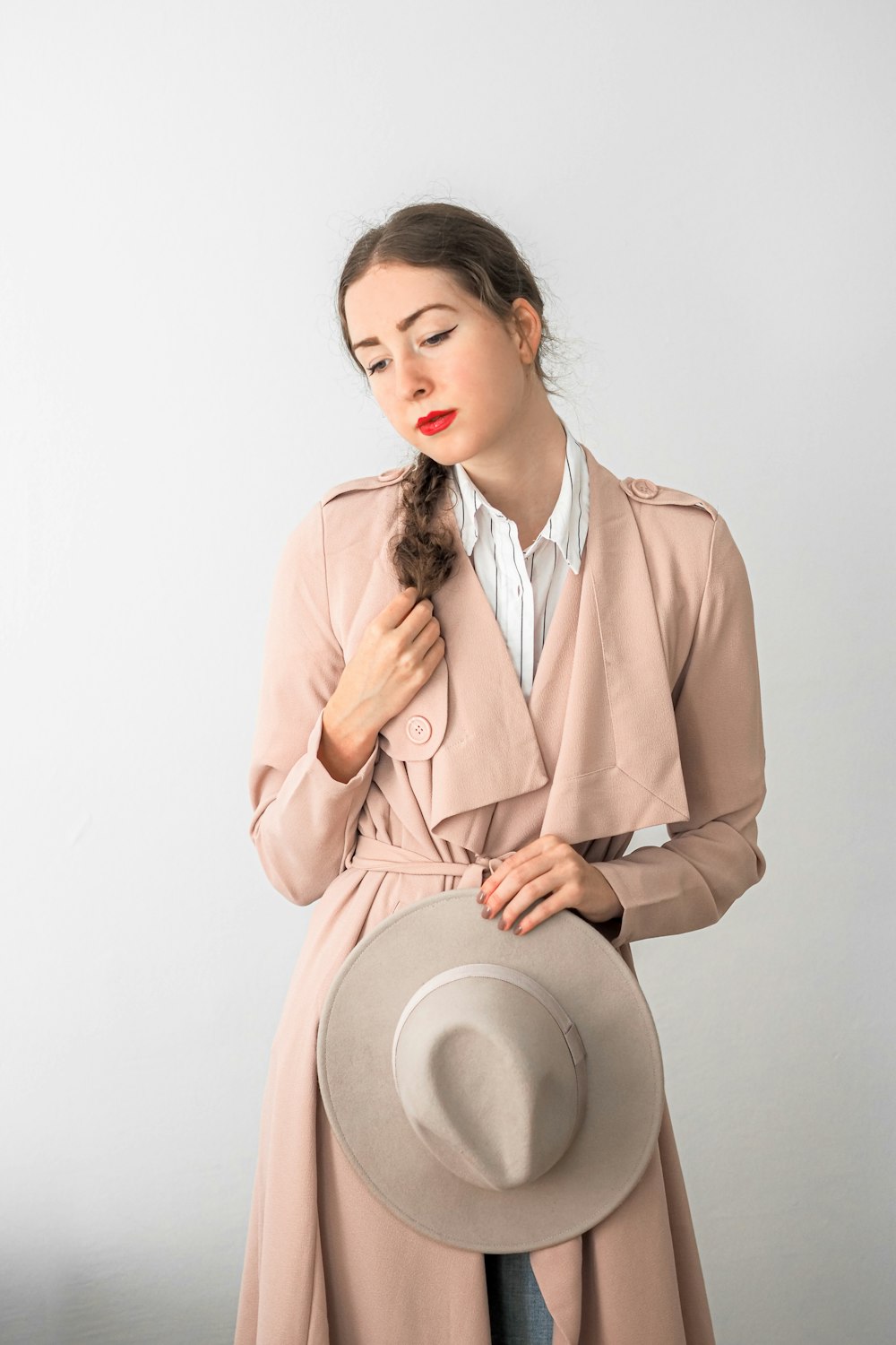 a woman in a trench coat holding a hat