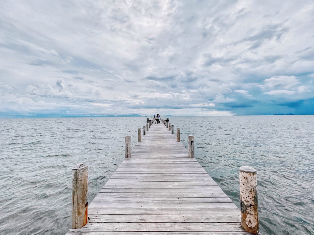 a wooden pier extending into the ocean under a cloudy sky