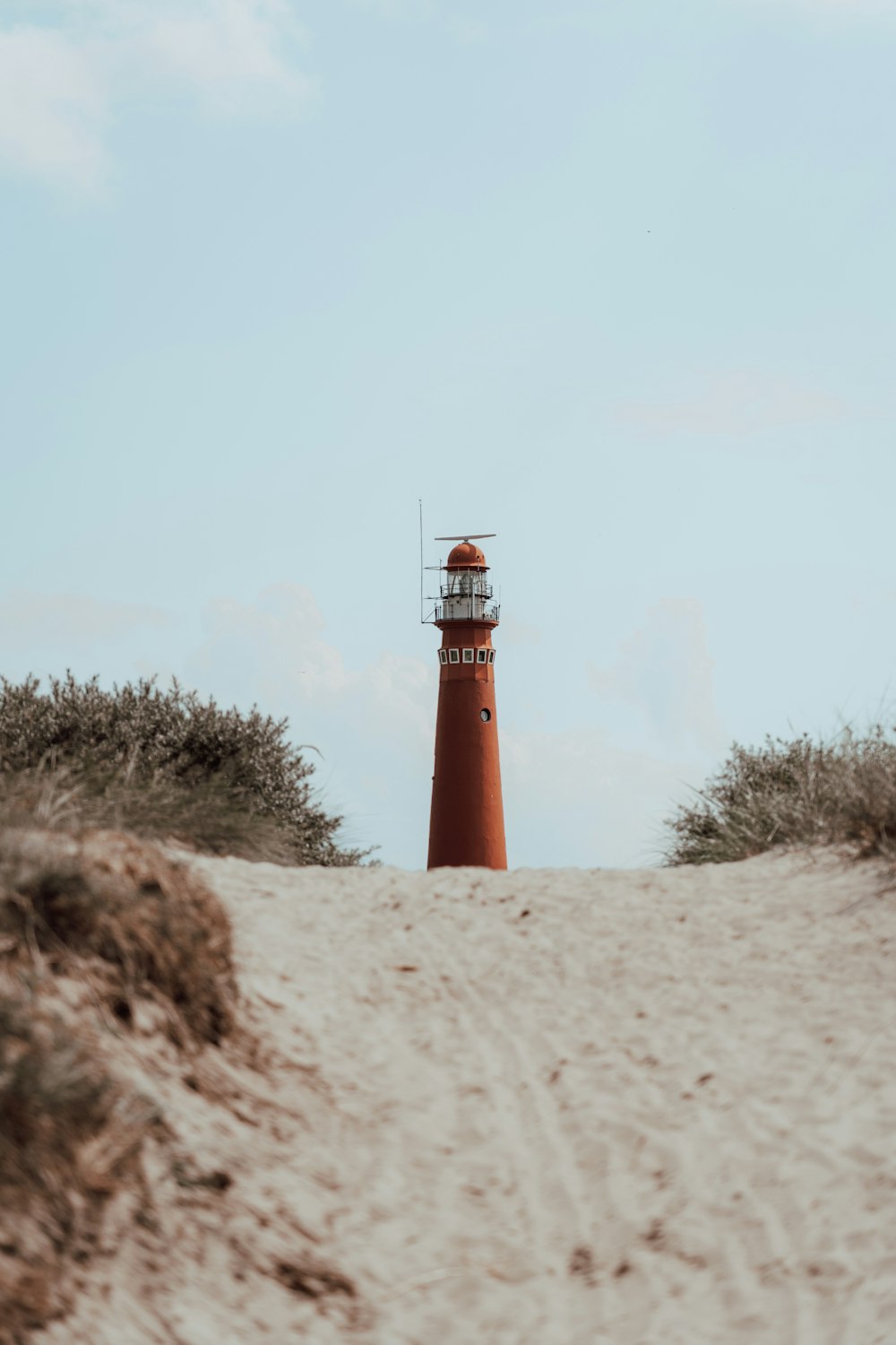 a red light house sitting on top of a sandy beach