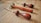 Three leatherworking tools with wooden handles rest on a wooden surface. The tools have curved metal tips and brass accents near the handles.